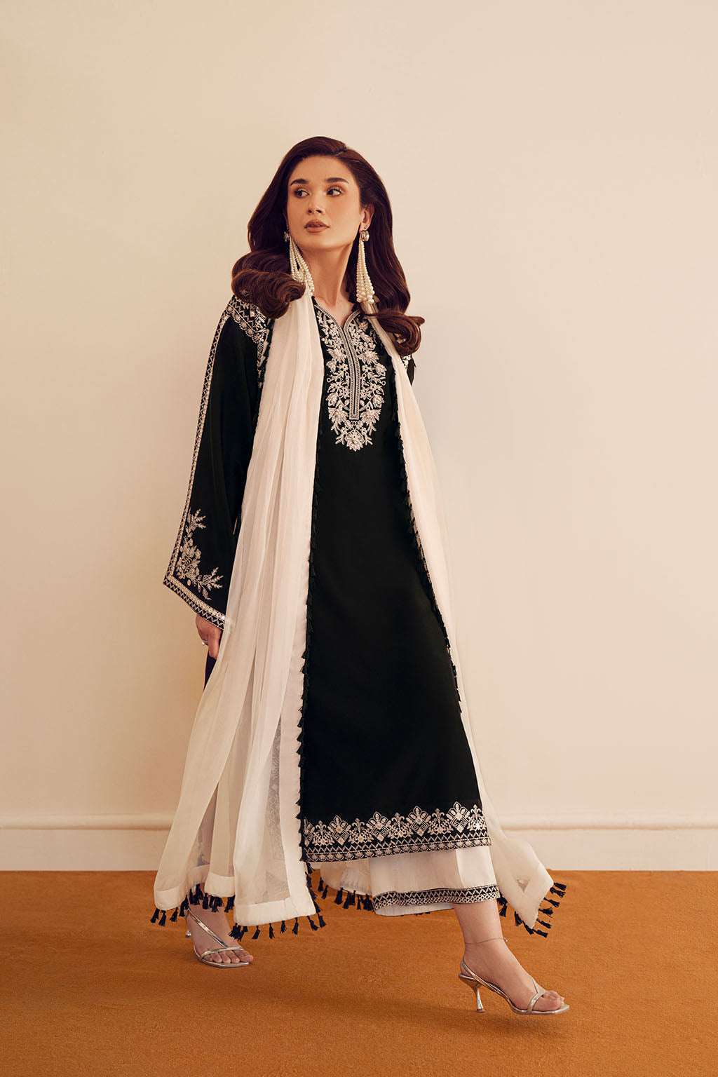Woman wearing a black and white embroidered traditional outfit with a white scarf on a beige background