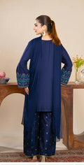 Woman wearing a navy blue traditional outfit with intricate patterns in a home setting.