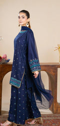 Woman wearing a navy blue traditional outfit with intricate patterns, sitting on a wooden chair.