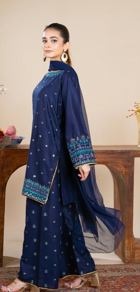Woman wearing a navy blue traditional outfit with intricate patterns, sitting on a wooden chair.
