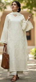 Woman wearing a white embroidered outfit with a brown bag outdoors.