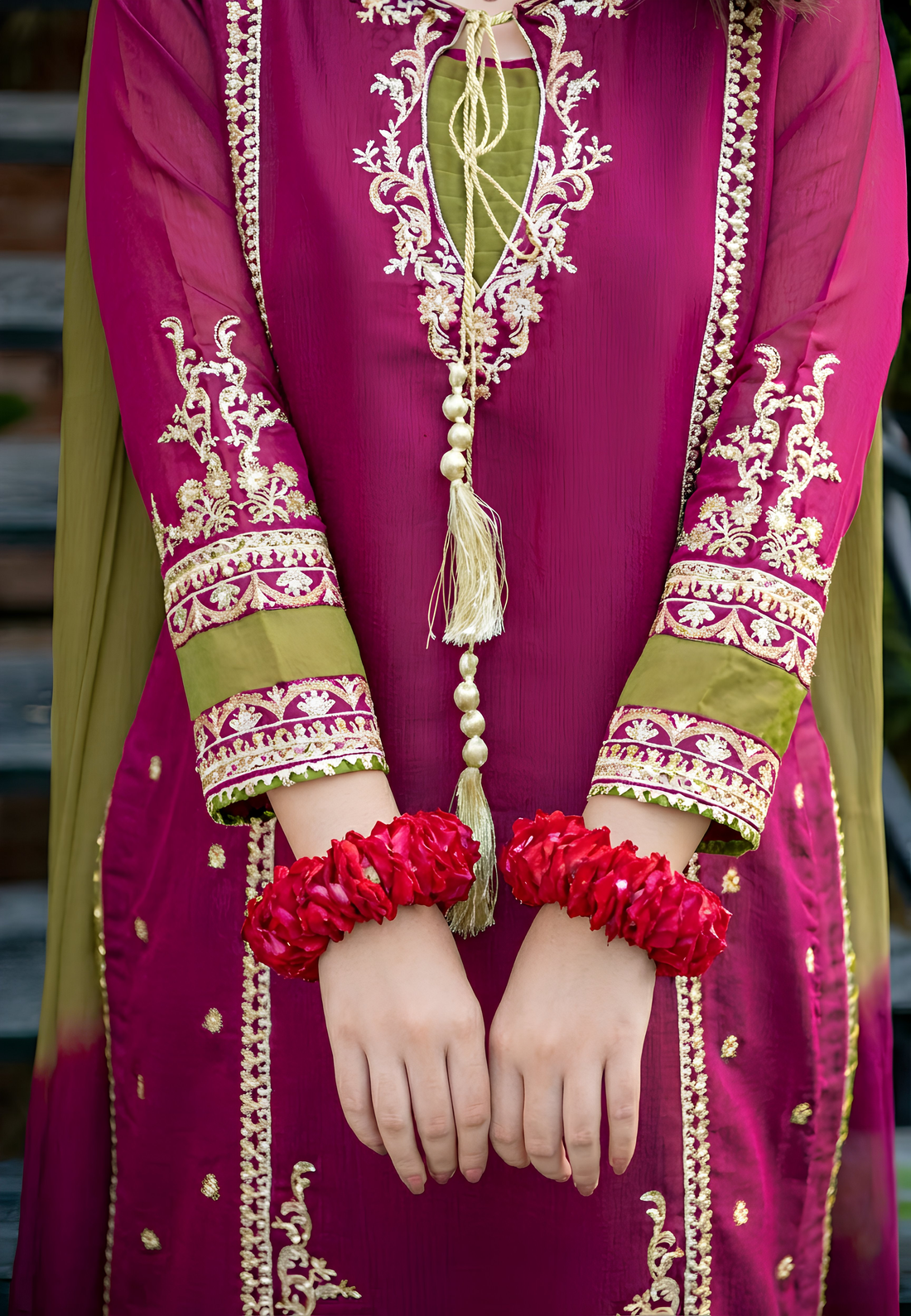 Person wearing a vibrant pink traditional outfit with intricate gold embroidery, holding red bangles.