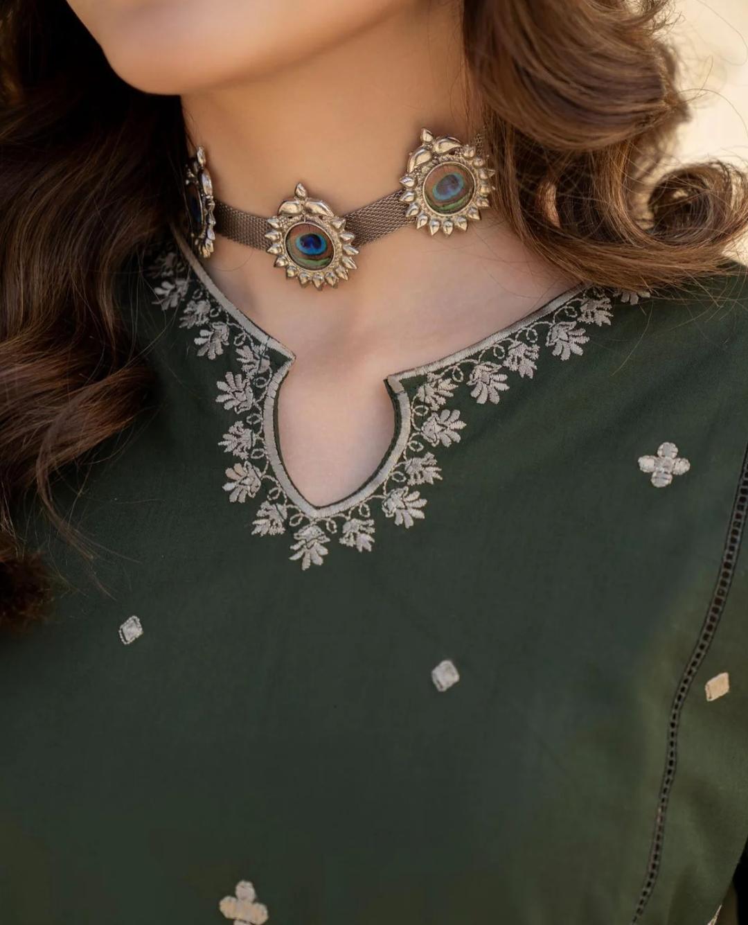 Close-up of a person wearing a green outfit with intricate silver embroidery and jewelry.