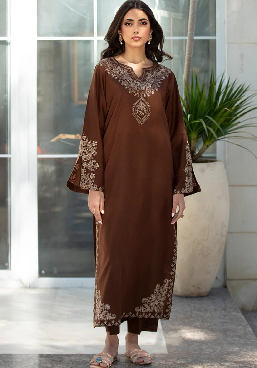 Woman wearing a brown embroidered outfit standing in front of a glass door.
