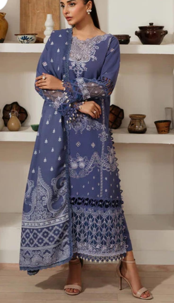 Woman wearing a blue embroidered outfit in a room with shelves displaying decorative items.