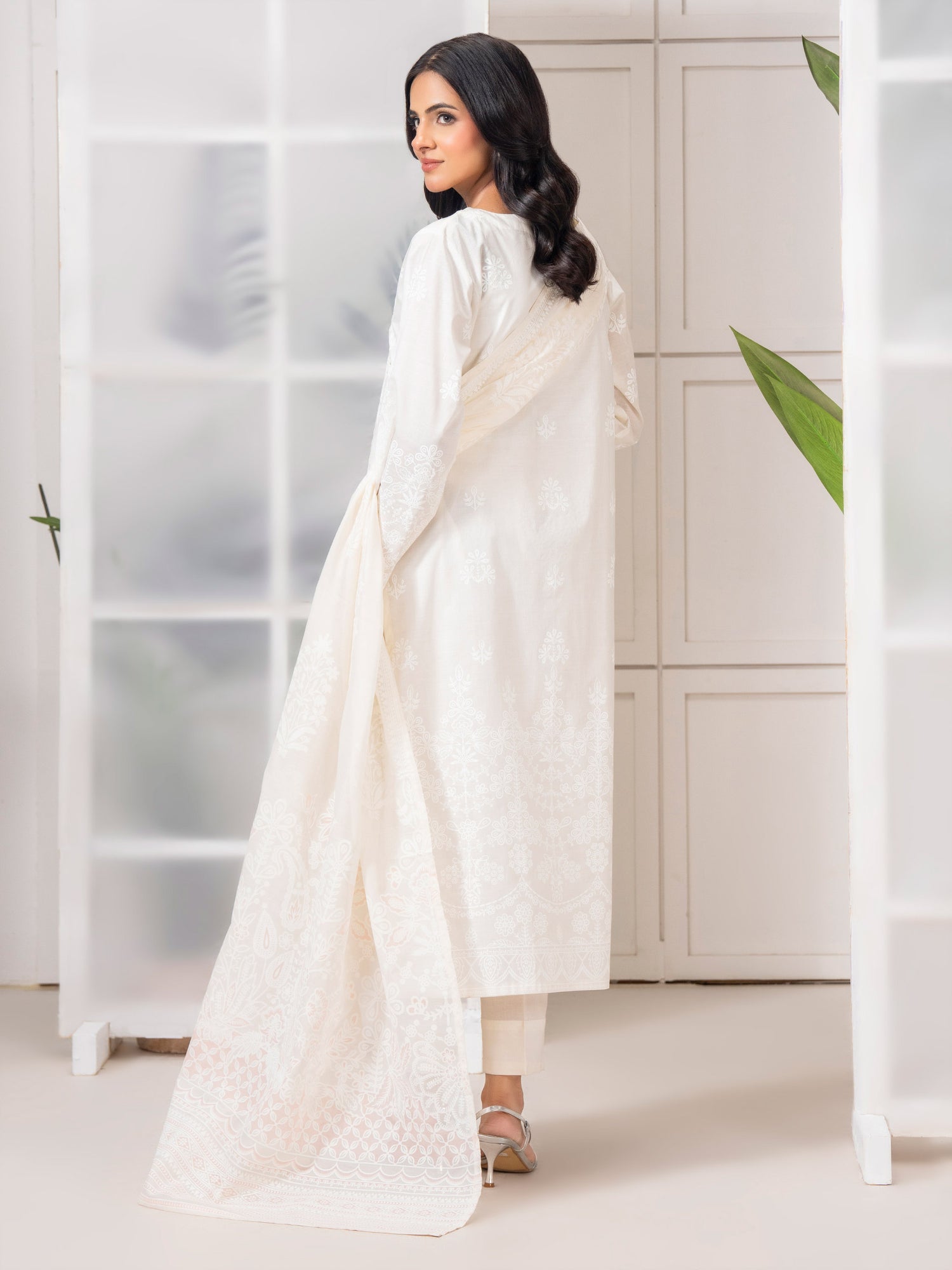 Woman in a white traditional outfit standing in a minimalistic room.