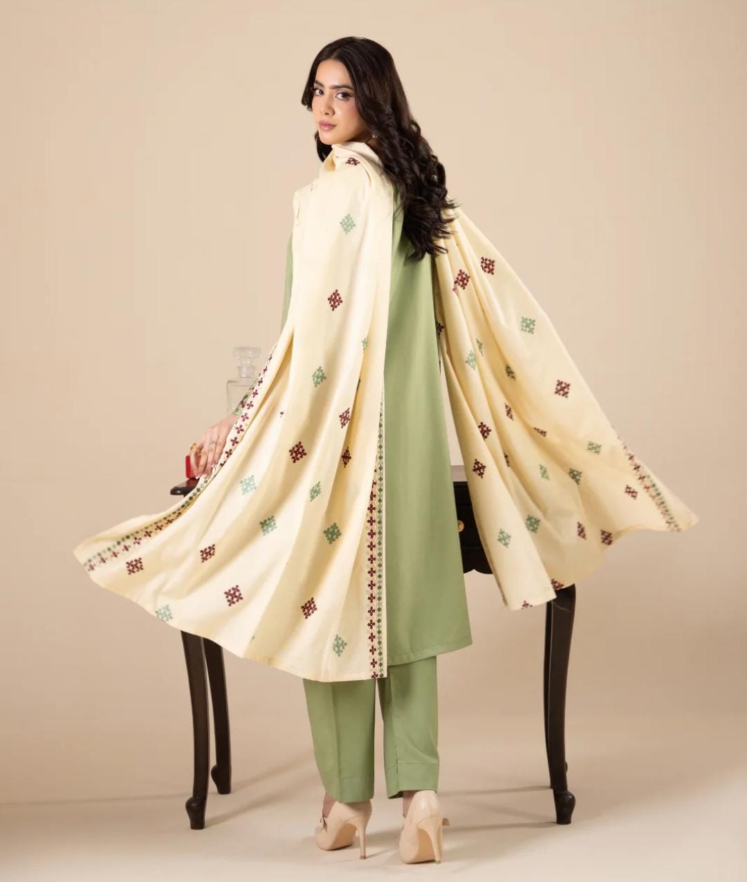 Woman wearing a traditional outfit with a cream dupatta and green pants on a beige background
