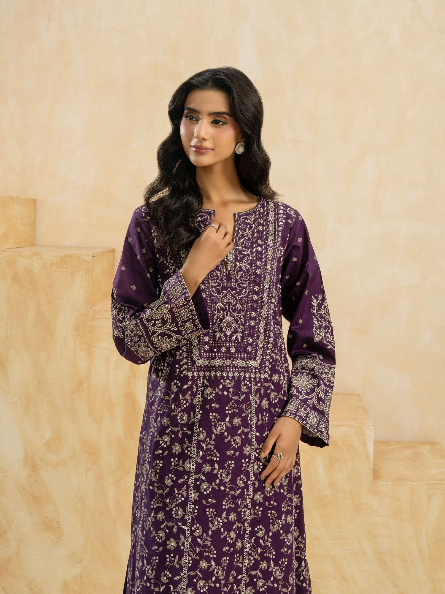 Woman wearing a purple patterned dress against a beige wall