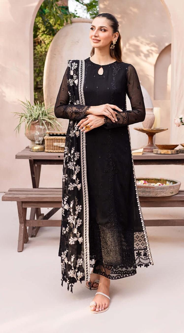 Woman in a black traditional outfit with floral patterns standing in an outdoor setting.