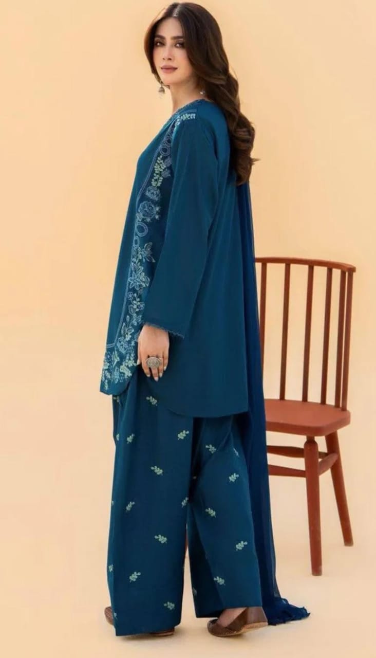 Woman wearing a blue embroidered outfit with a sheer dupatta on a beige background