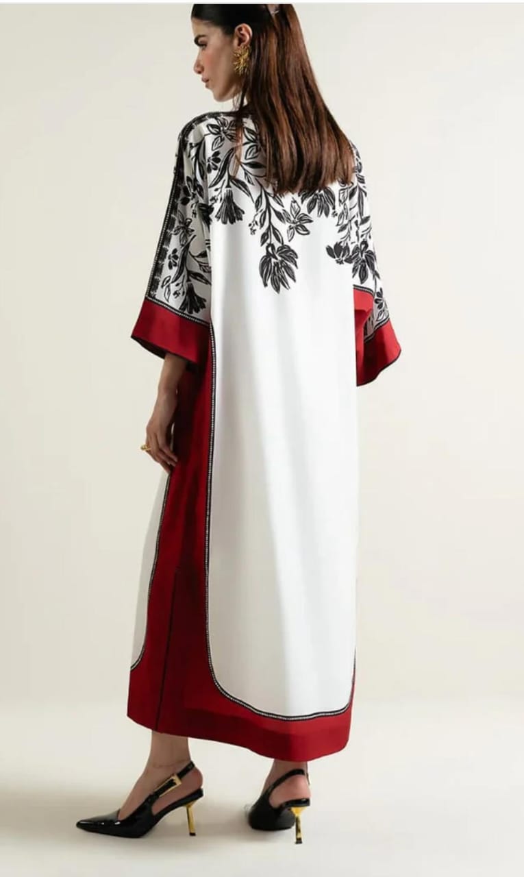 Woman wearing a white dress with black floral patterns and red accents on a plain background