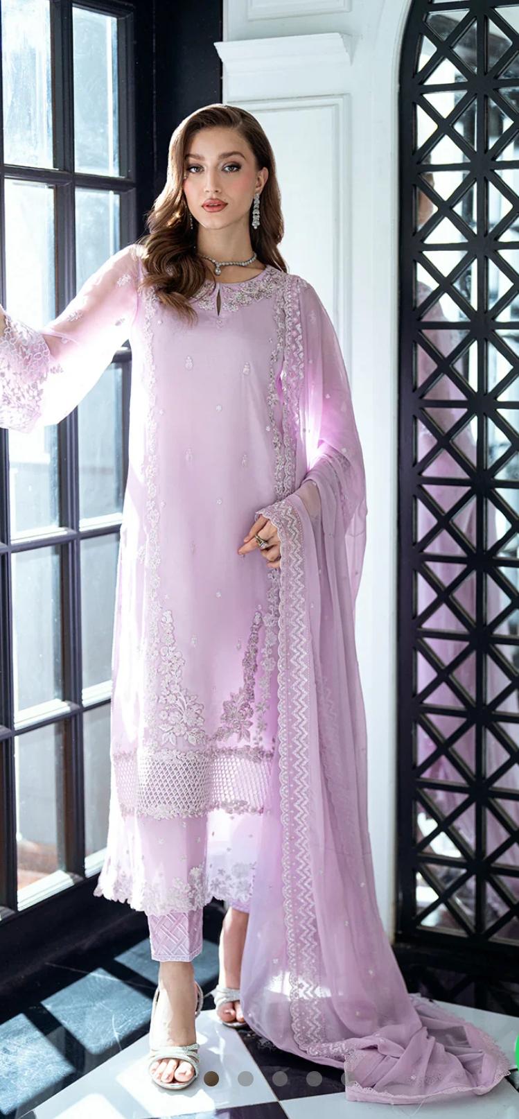 Woman wearing a light pink traditional outfit with intricate designs indoors.