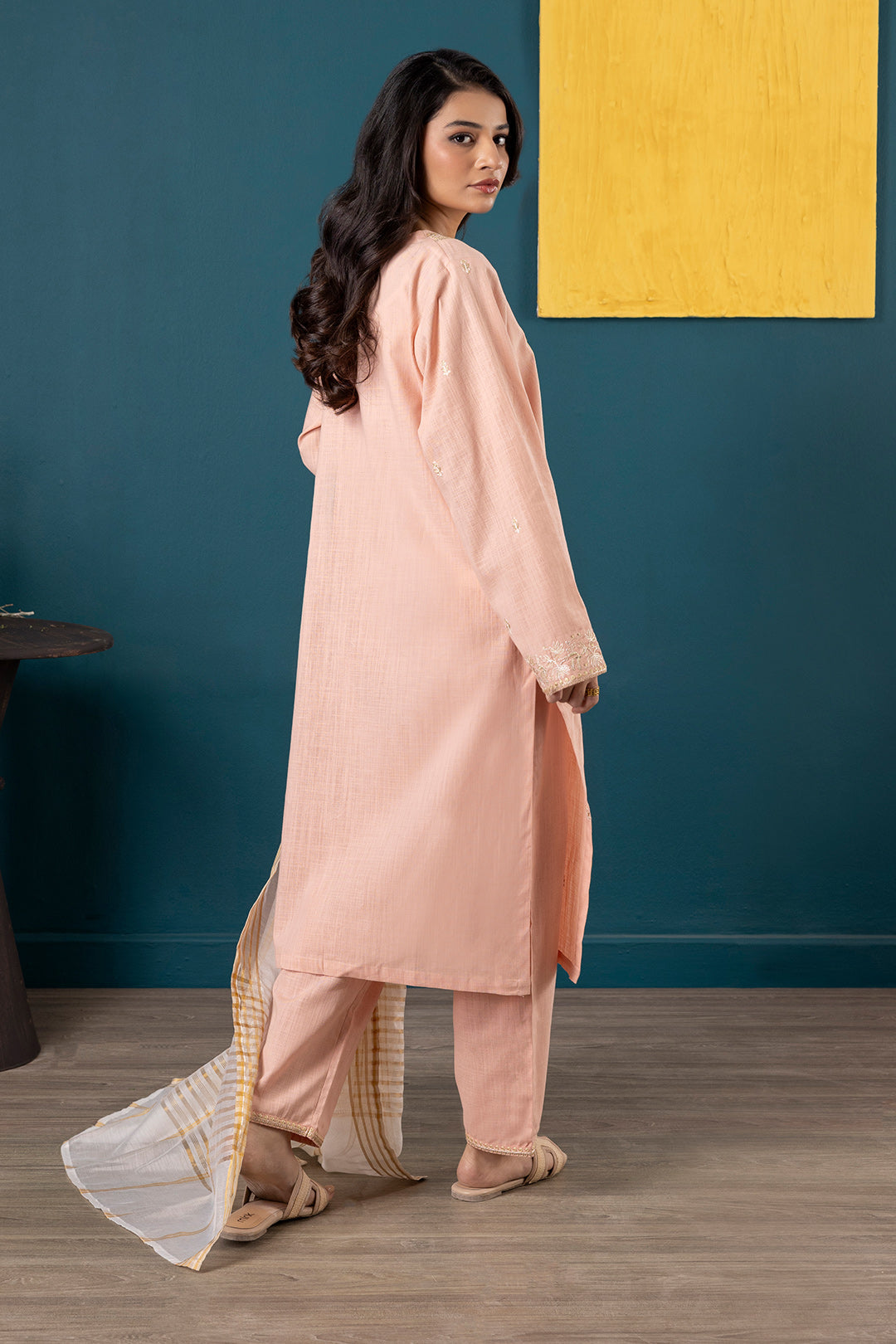 Woman wearing a peach traditional outfit against a blue wall with a yellow abstract painting.