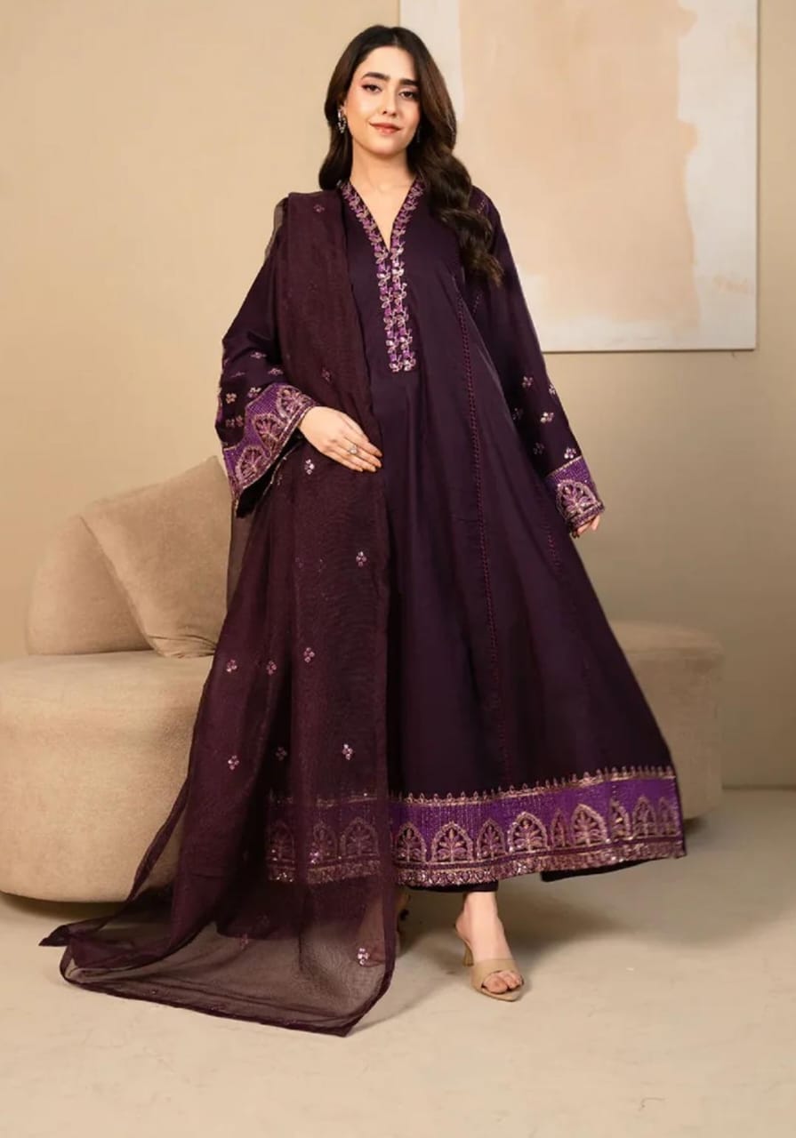 Woman wearing a dark purple embroidered outfit in a room with beige walls and furniture.