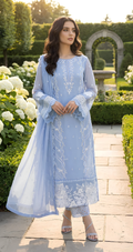 Woman in a light blue embroidered outfit standing in a garden.