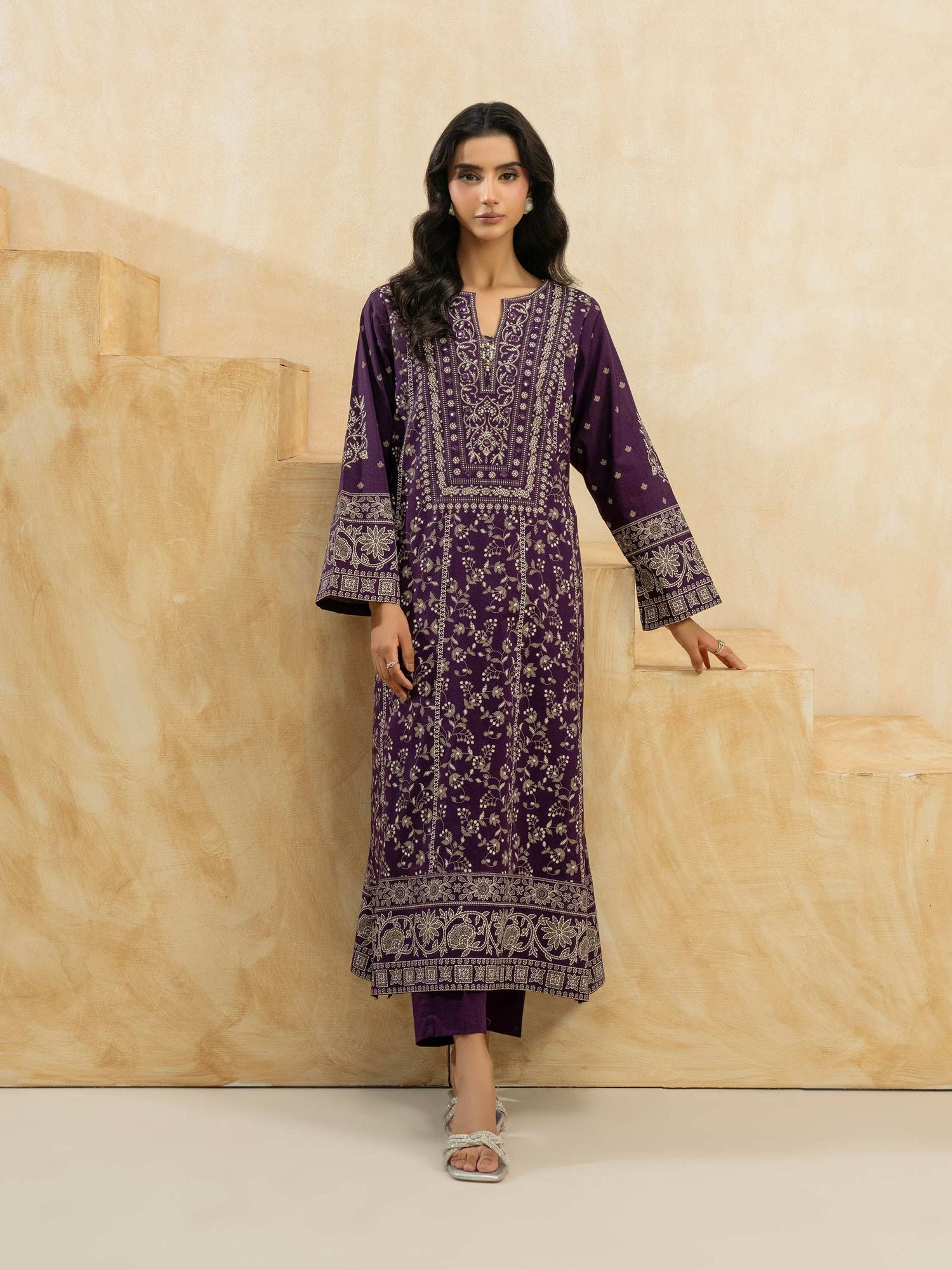 Woman wearing a purple embroidered outfit against a beige background