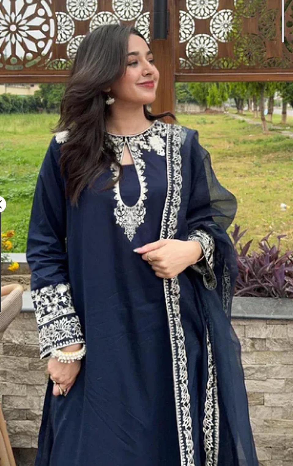 Woman wearing a navy blue traditional outfit with white embroidery in an outdoor setting.