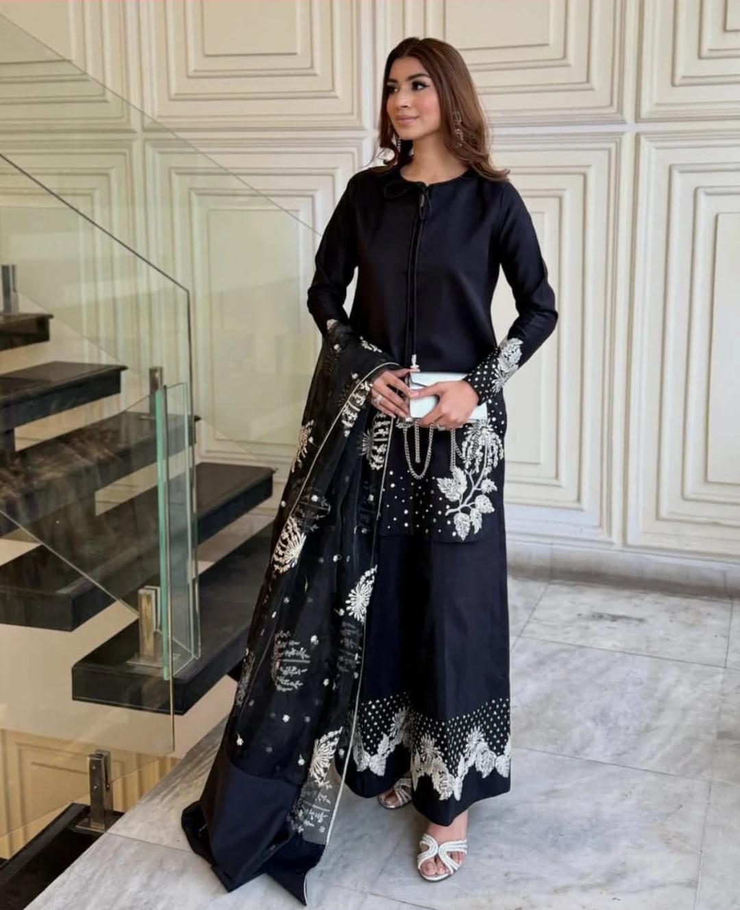 Woman in a black outfit with white patterns standing in an elegant interior setting.