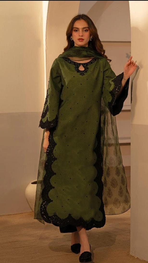Woman wearing a green and black traditional outfit with a scarf indoors.