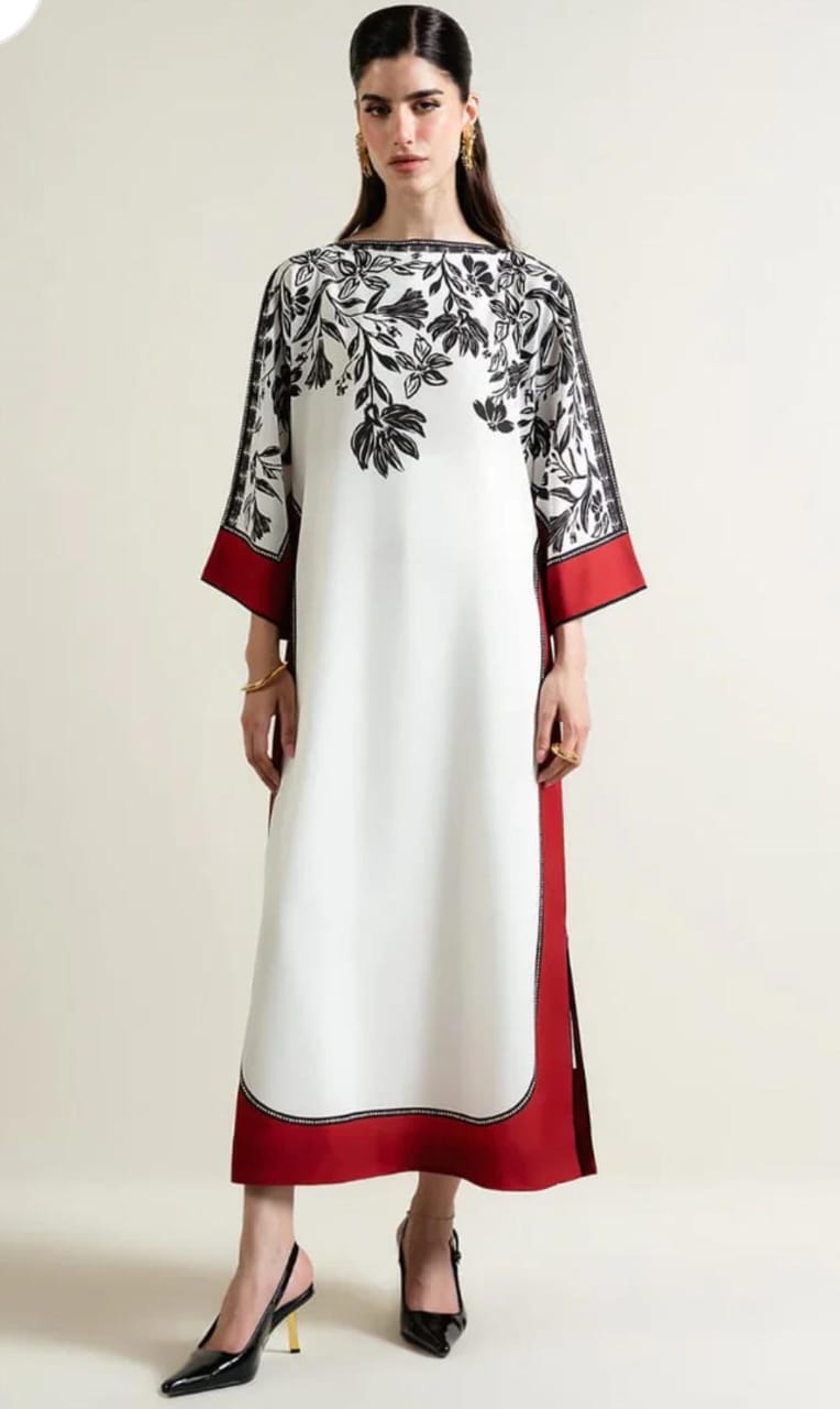 Woman wearing a white dress with black floral patterns and red accents on a plain background