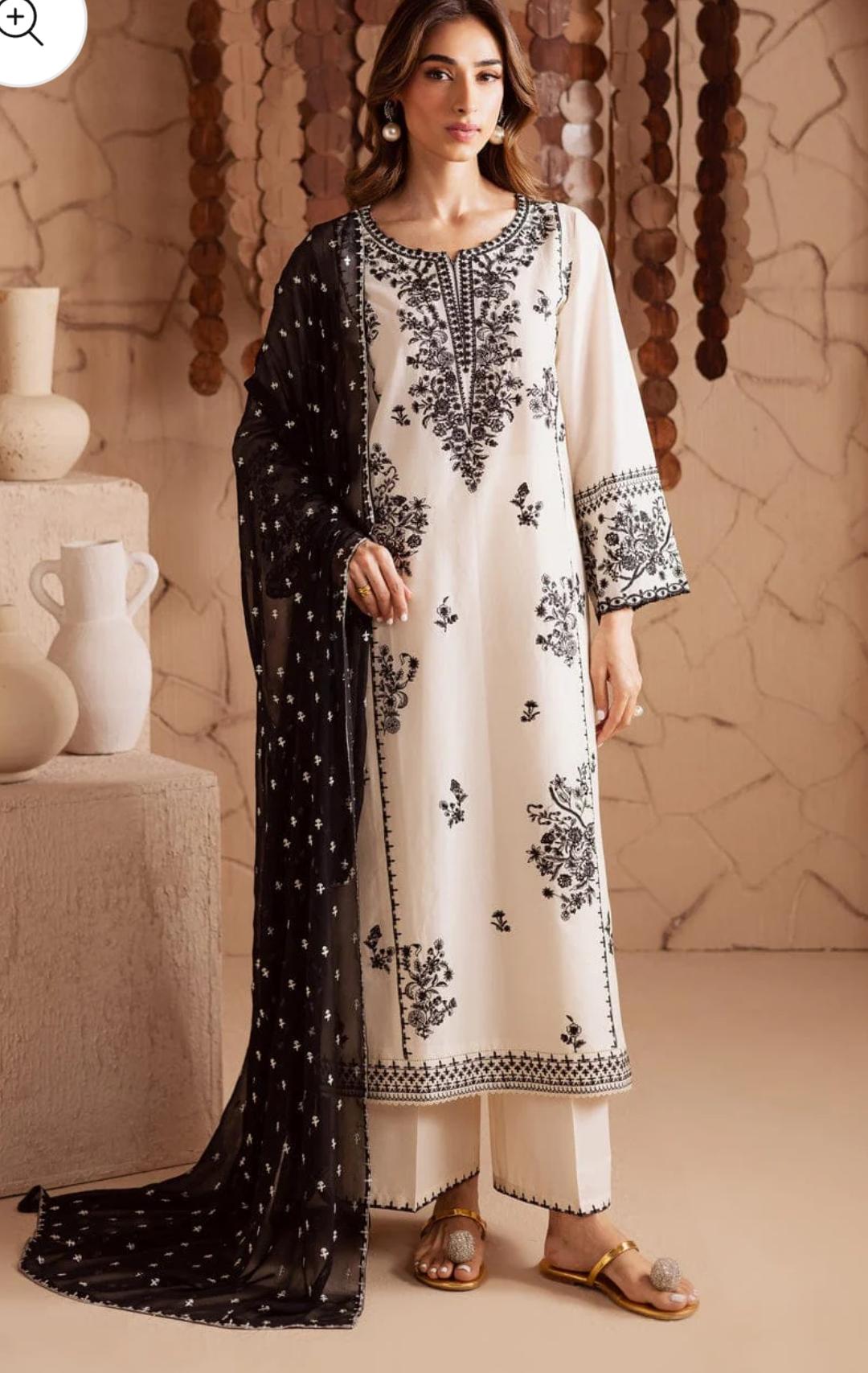 Woman wearing a white and black embroidered outfit with a black dupatta in a decorative setting.