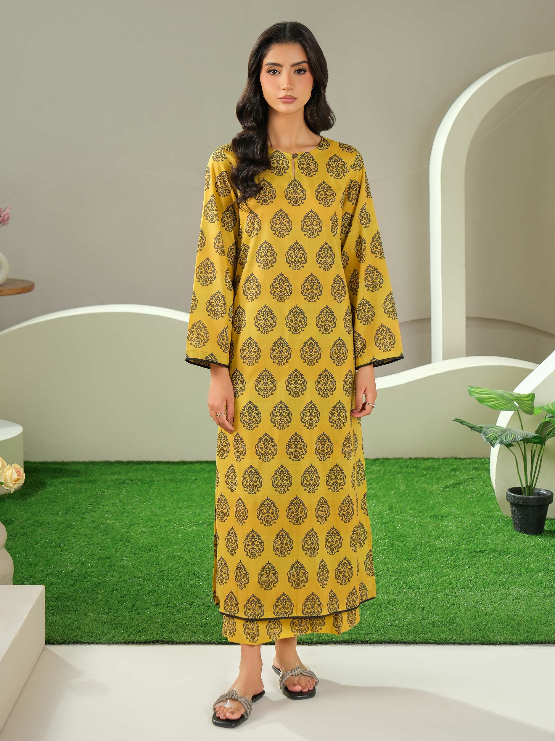 Woman wearing a yellow patterned outfit standing in a decorative indoor setting.