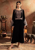 Woman in a black embroidered dress standing in an ornate room with a decorative background.