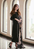 Woman in a black dress with lace details standing in a room with large windows.