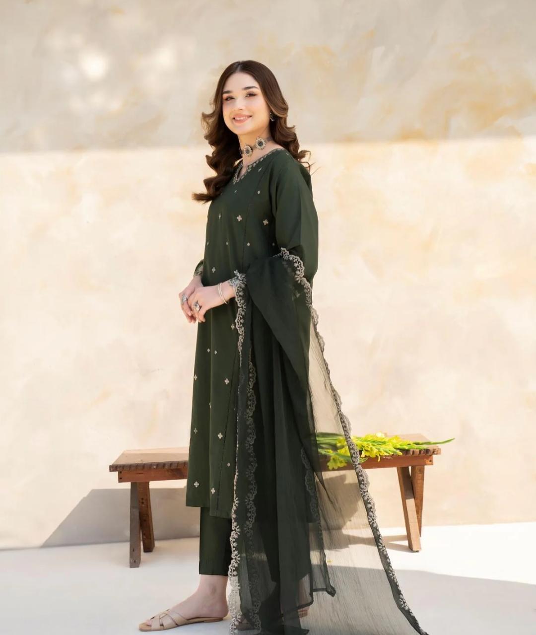 Woman in a green traditional outfit with a sheer dupatta against a neutral background