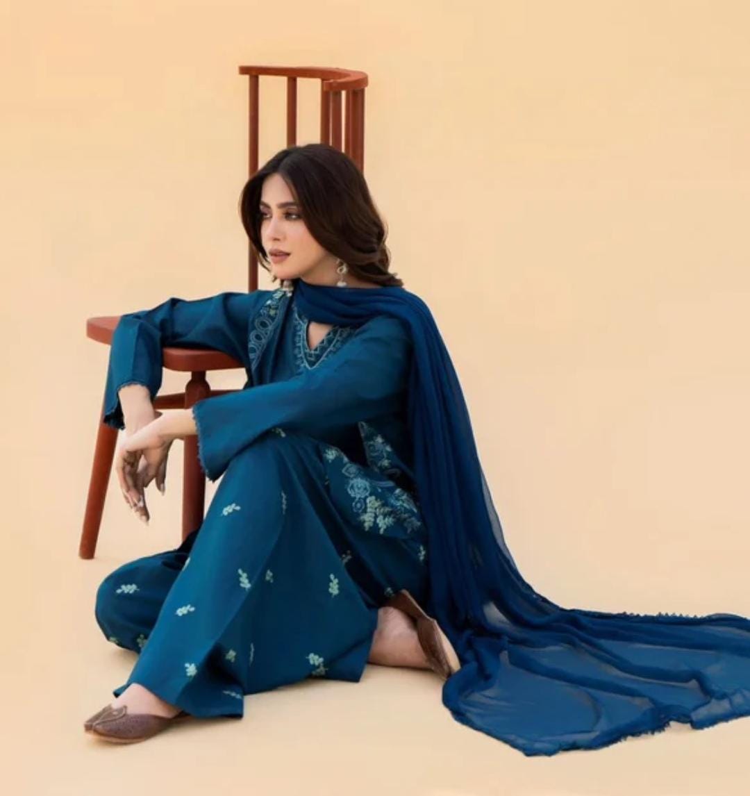 Woman in a blue traditional outfit sitting on a chair against a beige background