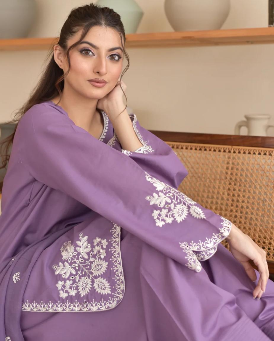 Woman wearing a purple outfit with white embroidery sitting on a couch.