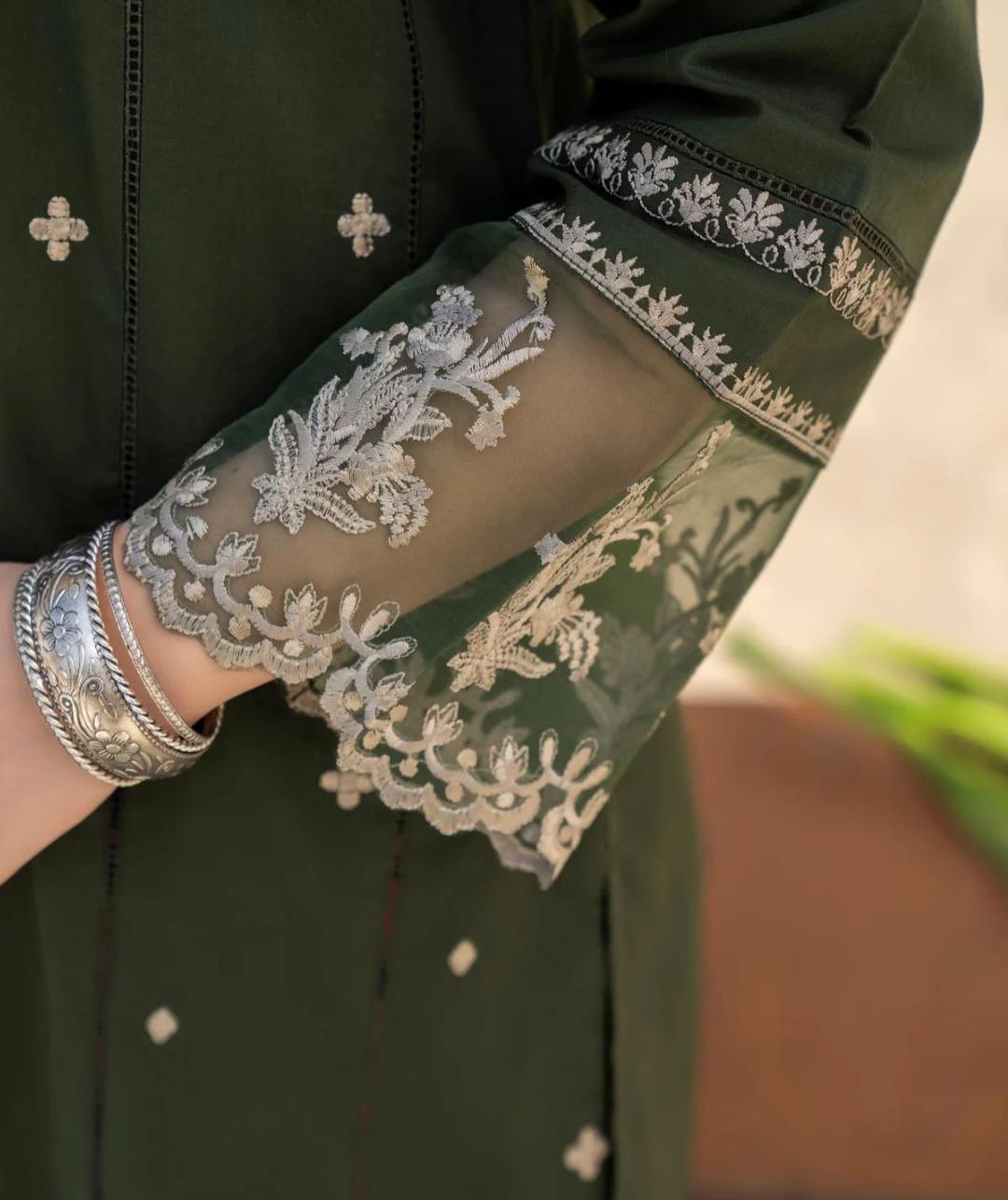 Green garment with silver embroidery and a person wearing silver bangles.