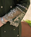 Green garment with silver embroidery and a person wearing silver bangles.