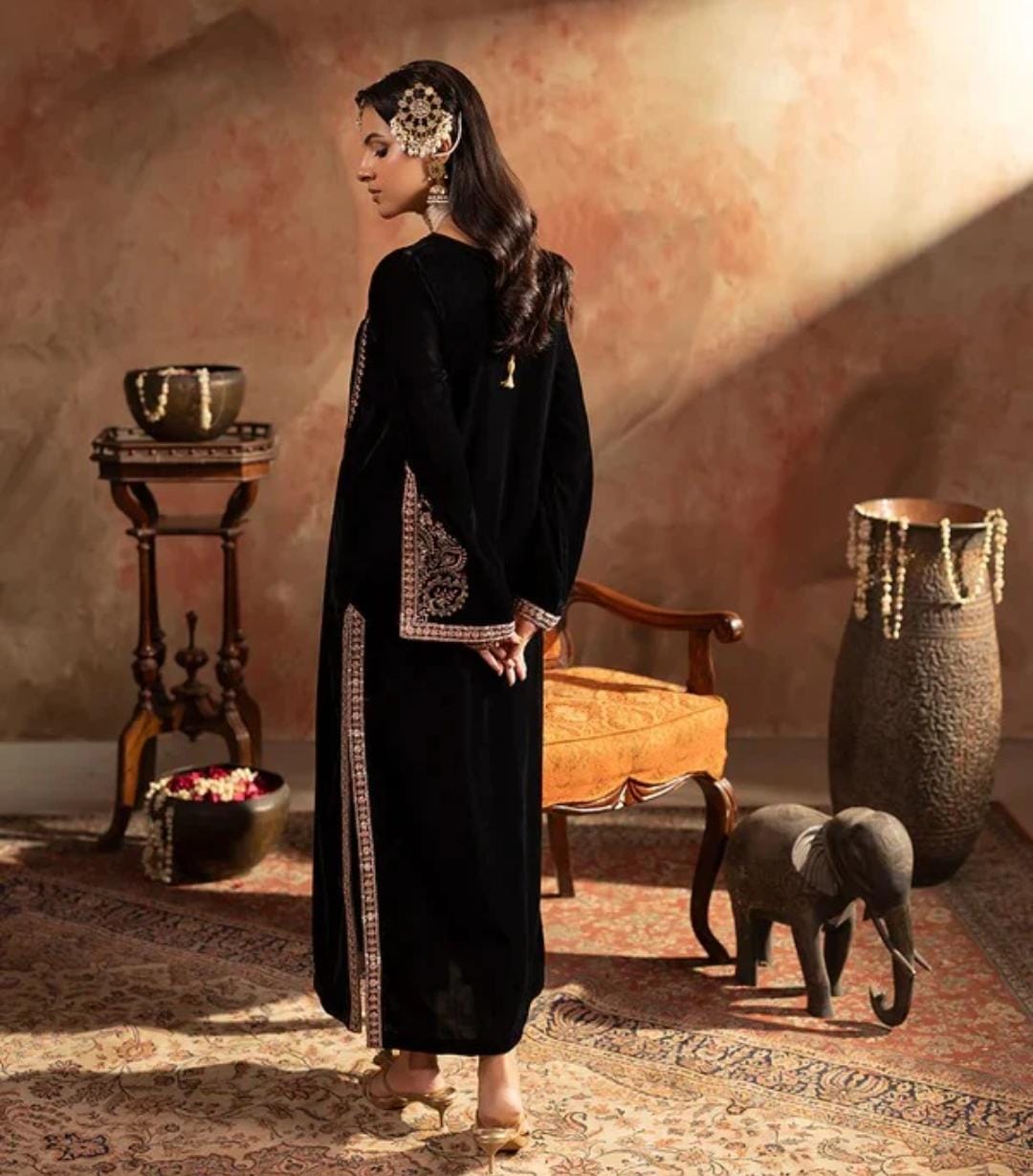 Woman in a black embroidered dress standing in a room with decorative elements and an elephant model.