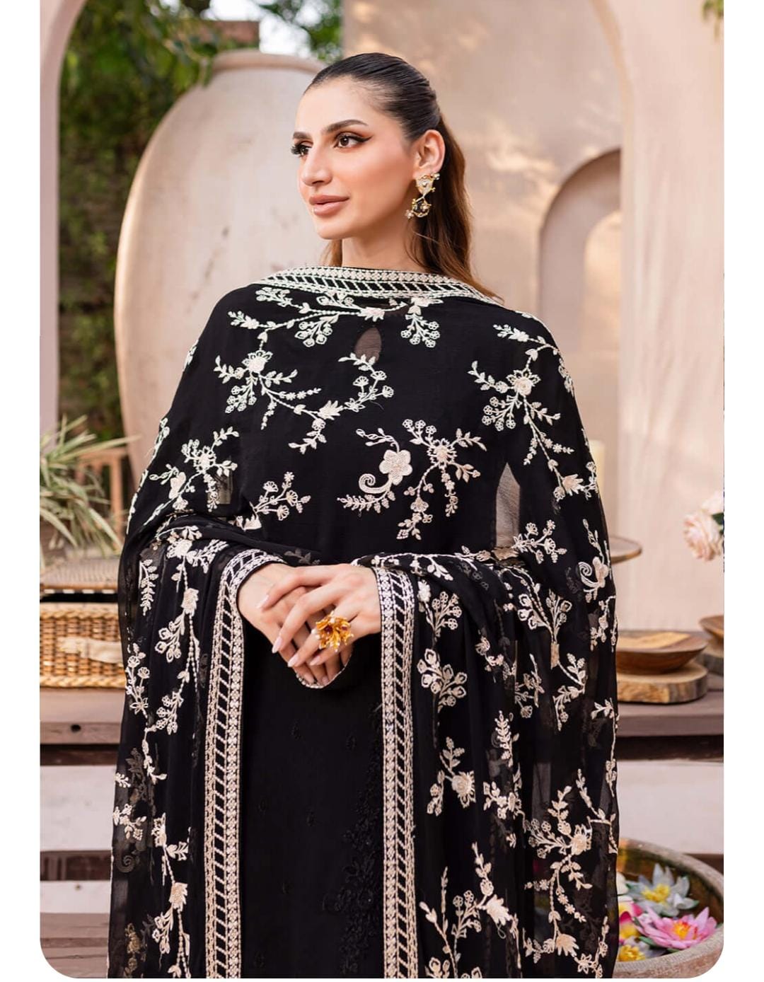 Woman wearing a black embroidered outfit with floral patterns in an outdoor setting.