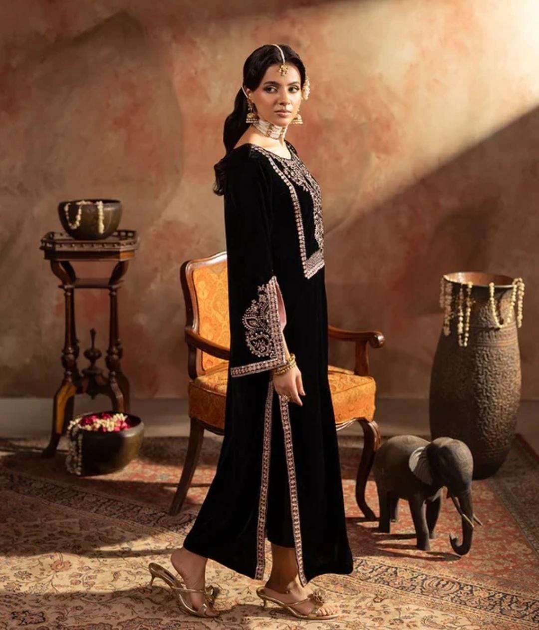 Woman in a black traditional outfit with intricate designs in a decorative room.