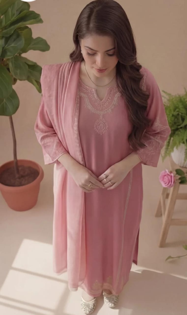 Woman in a pink dress with a matching jacket standing indoors with plants around.