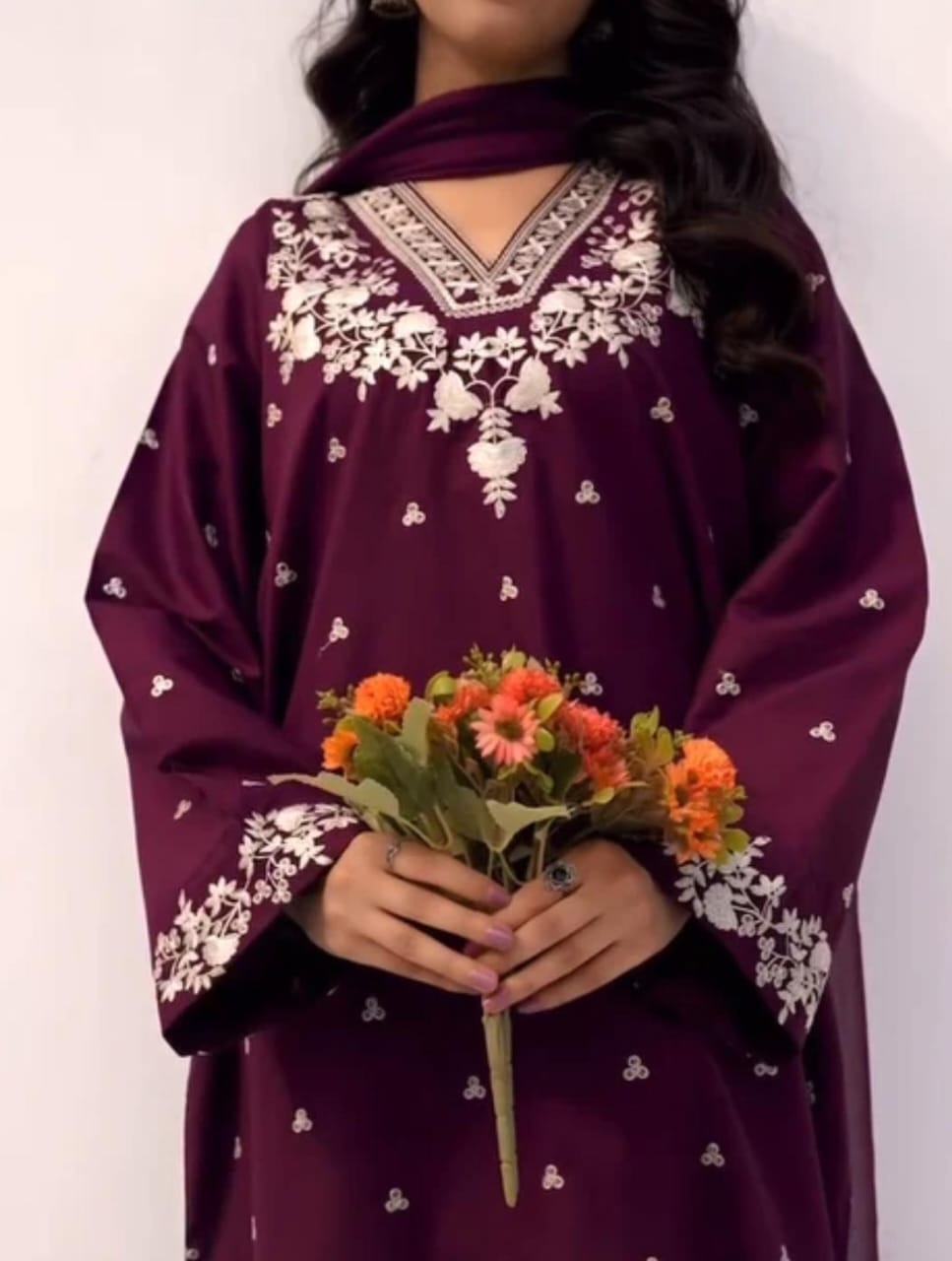 Person wearing a purple embroidered outfit holding flowers against a white background