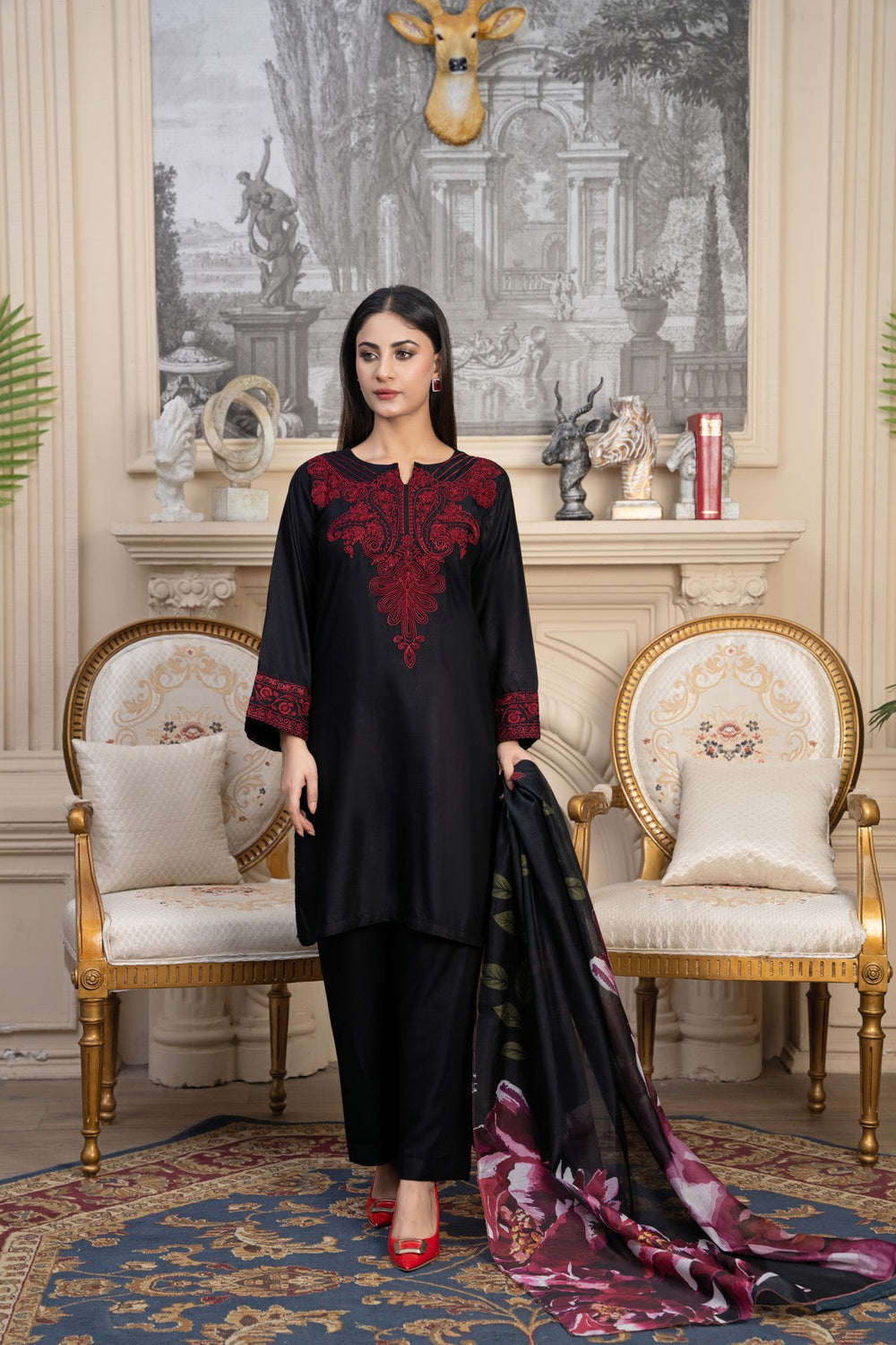 Woman in black and red traditional outfit with a patterned scarf in an elegant room.