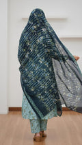 Person wearing a floral shawl over their head in a minimal indoor setting