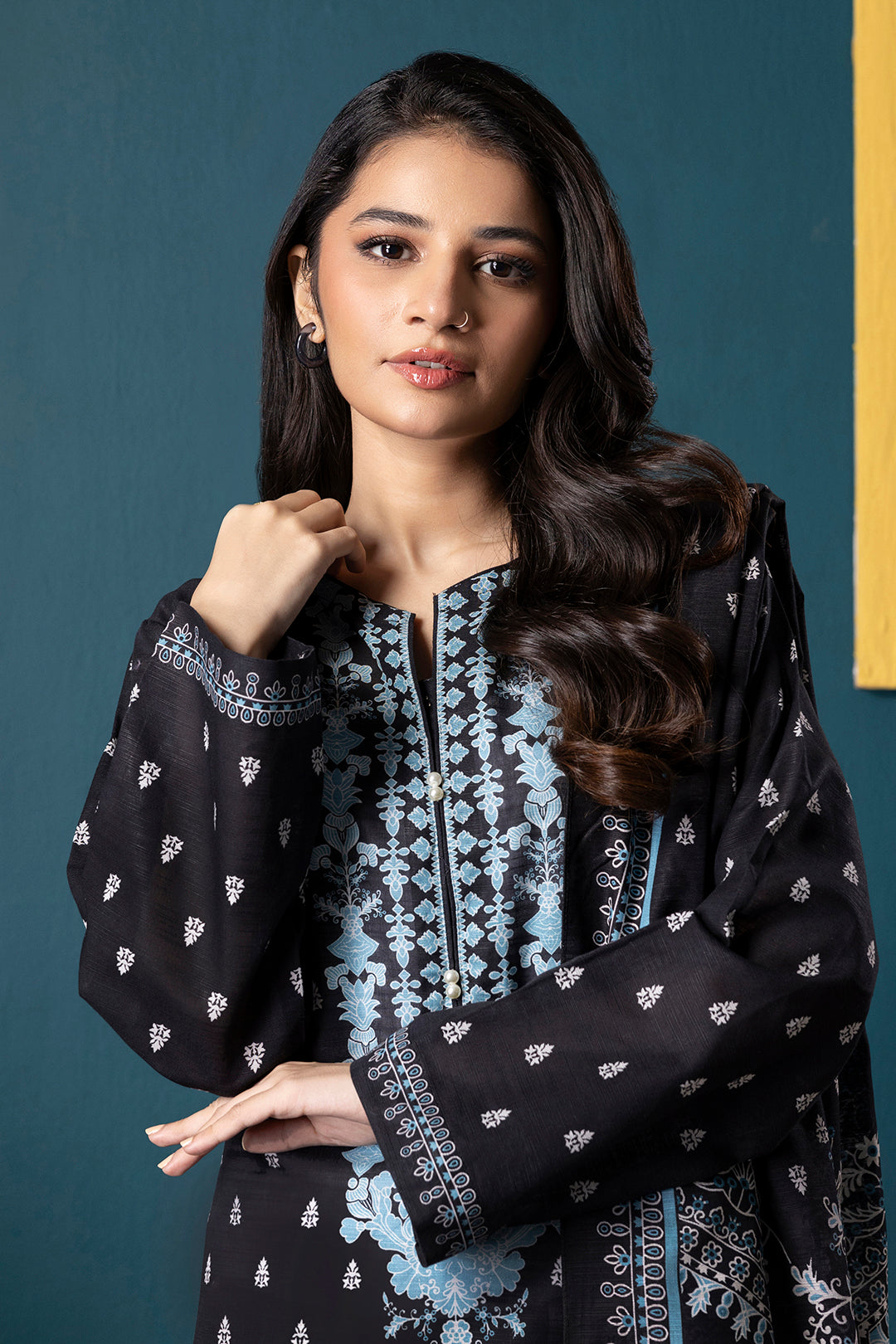 Woman wearing a black and blue patterned outfit against a teal wall.