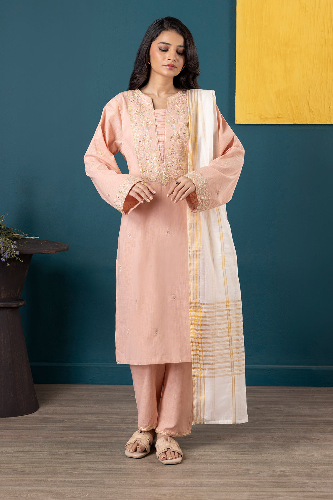 Woman in a pink traditional outfit with a white scarf against a blue wall.