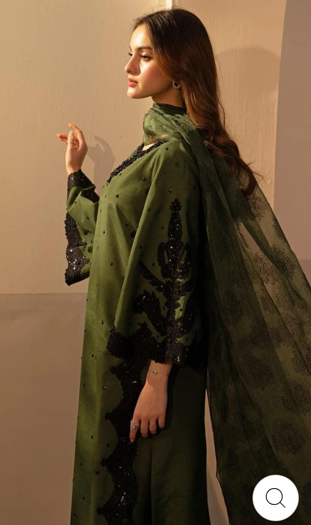 Woman wearing a green traditional outfit with black embroidery against a plain background