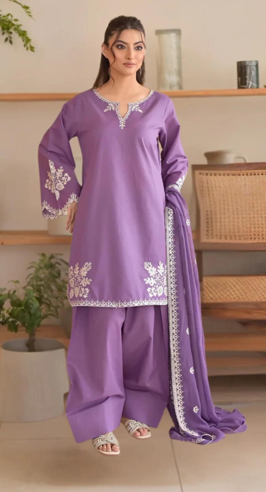 Woman wearing a purple traditional outfit with white embroidery in a home setting.