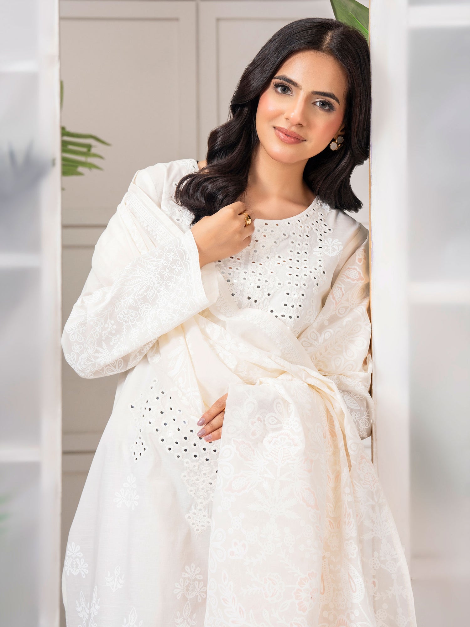 Woman wearing a white dress with intricate patterns in a neutral setting