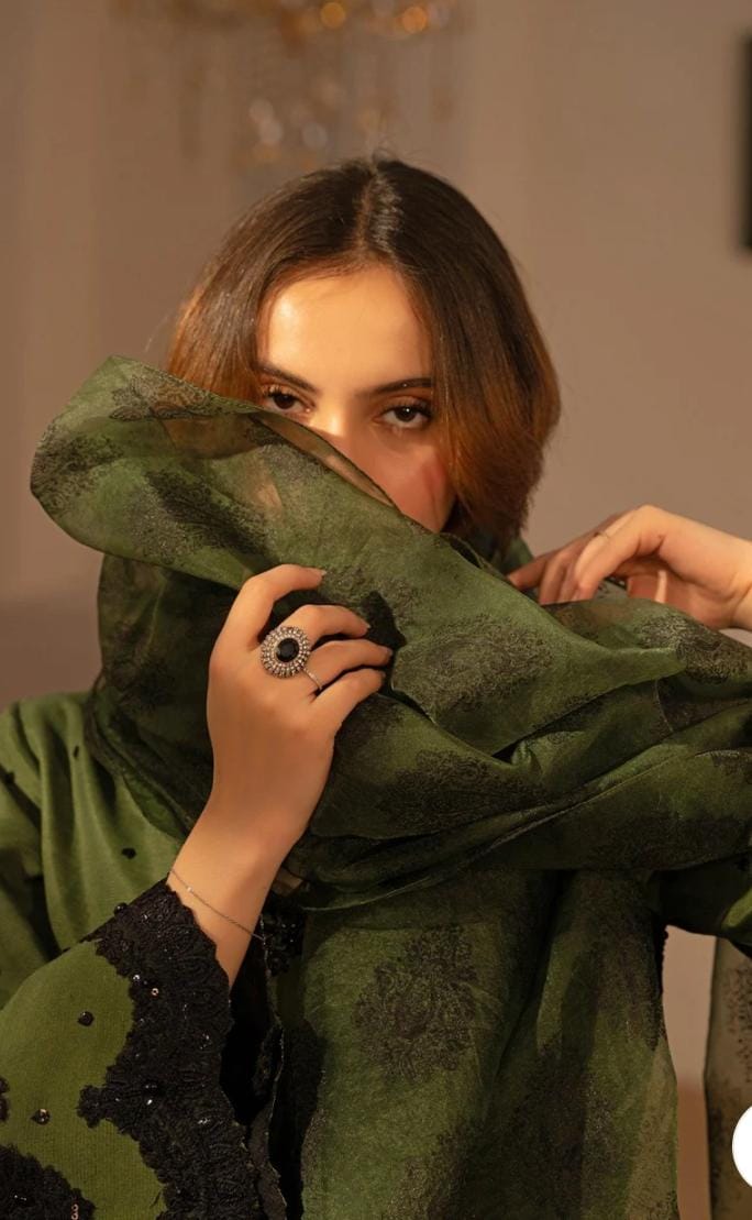 Woman wearing a green and black traditional outfit in an indoor setting.