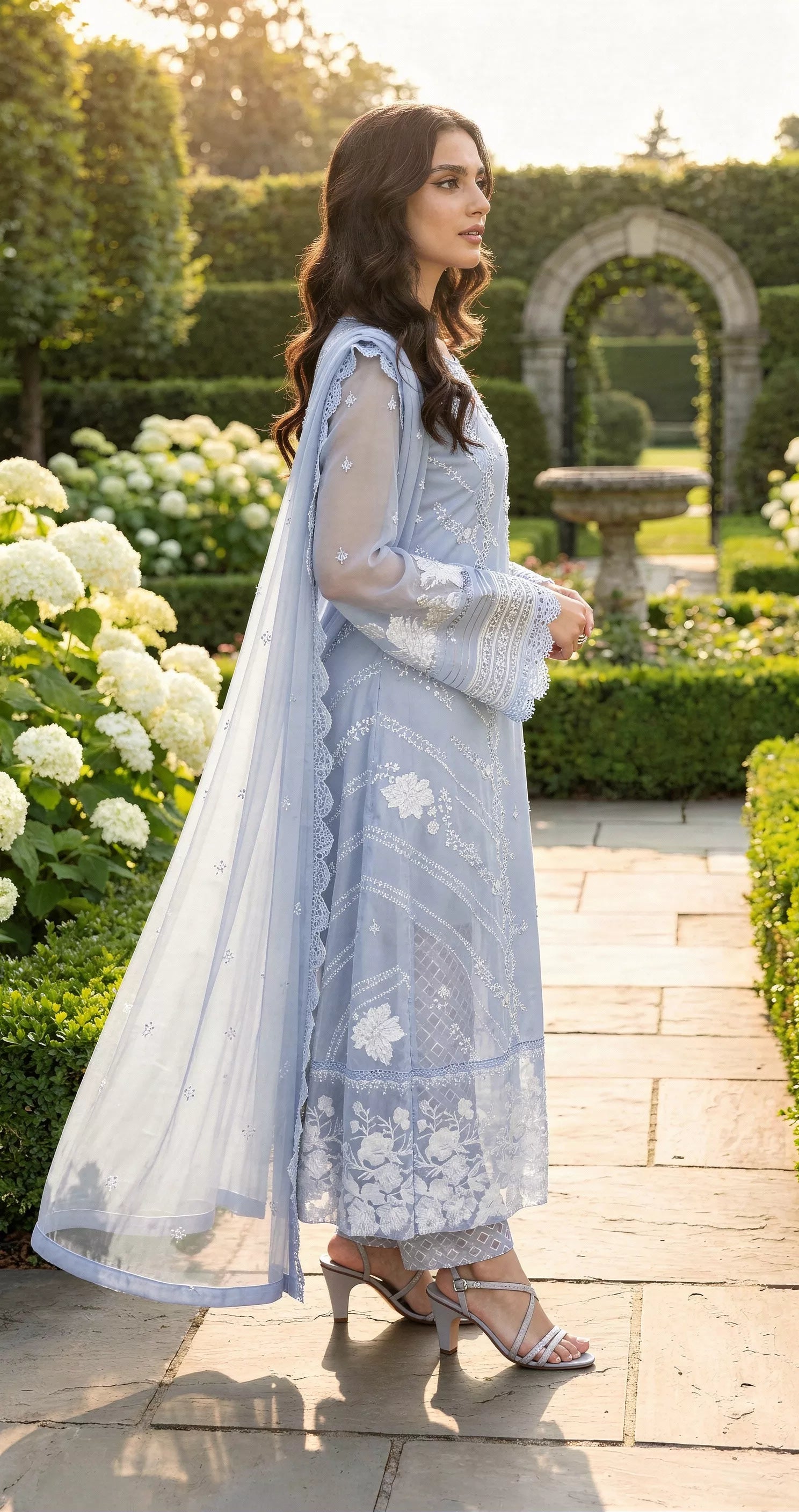 Woman in a light blue traditional outfit standing in a garden.