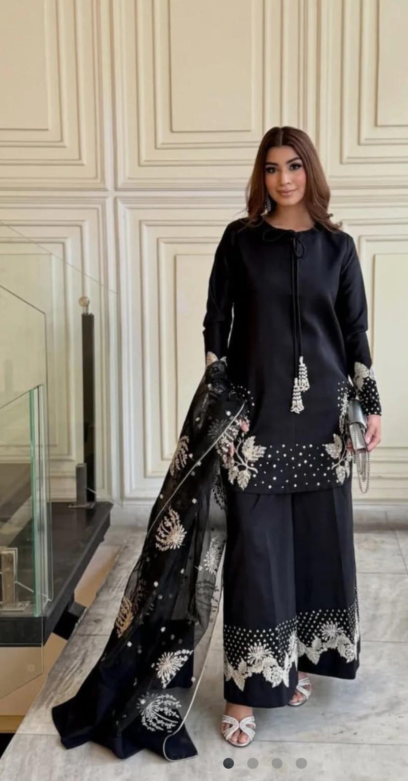 Woman in a black outfit with floral patterns standing indoors.