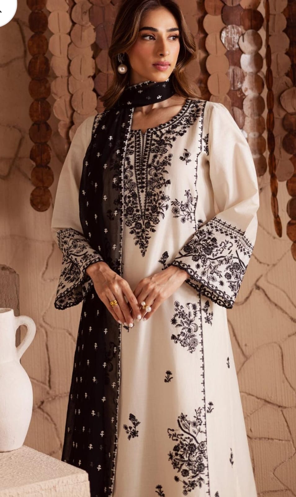 Woman wearing a white dress with black embroidery in an indoor setting.