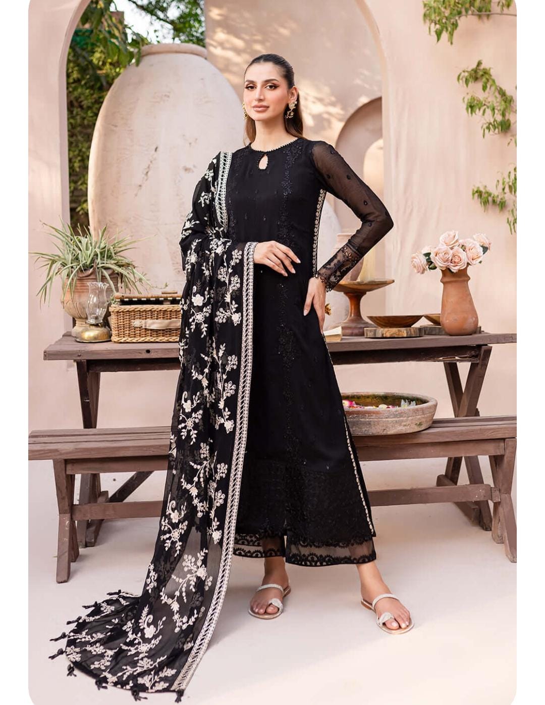 Woman in a black traditional outfit with floral patterns standing in an outdoor setting.